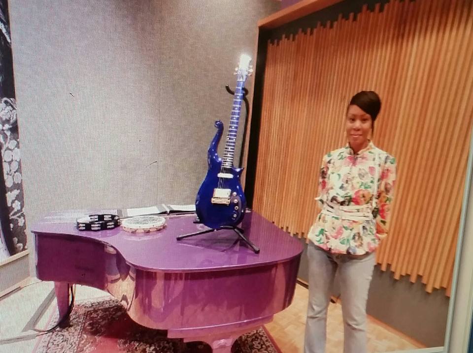 Tammy Sharpe standing in front of one of Prince's pianos and guitars at Paisley Park.